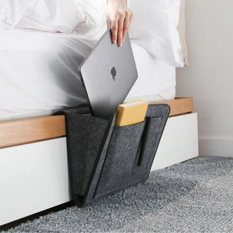 Gray felt storage organizer hanging on the side of a couch with magazines, a remote, and phone inside.
