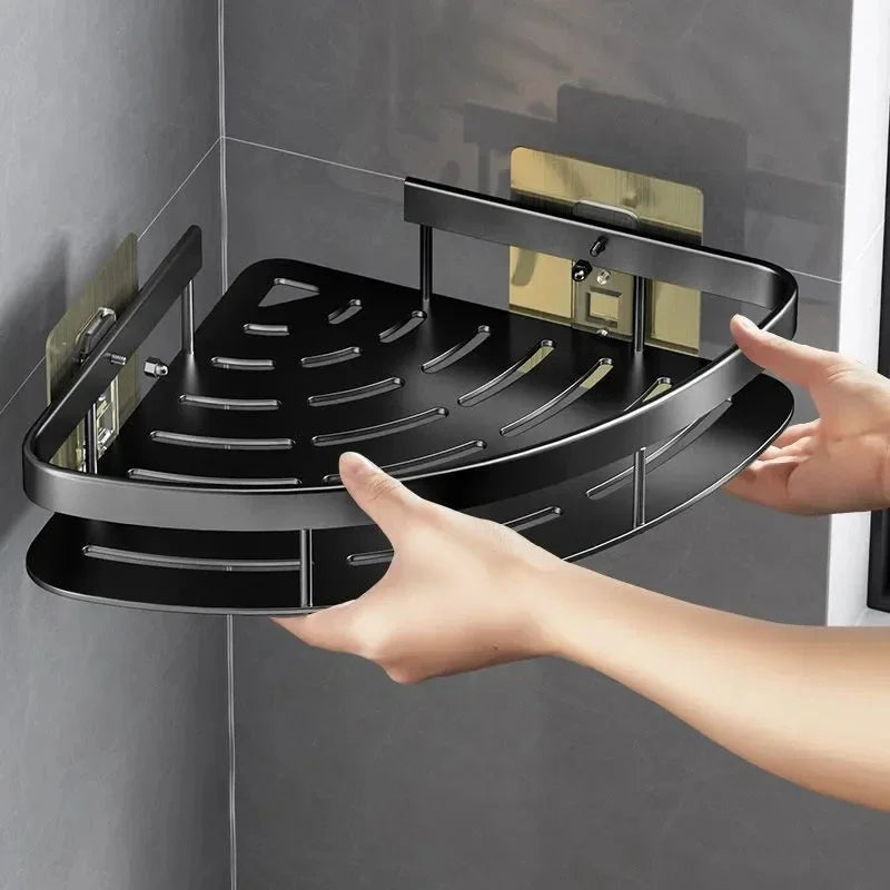 Black corner shower caddy being held by a person against a gray tiled wall.
